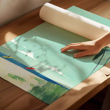 Person rolling out a green placemat with a scenic design on a wooden surface