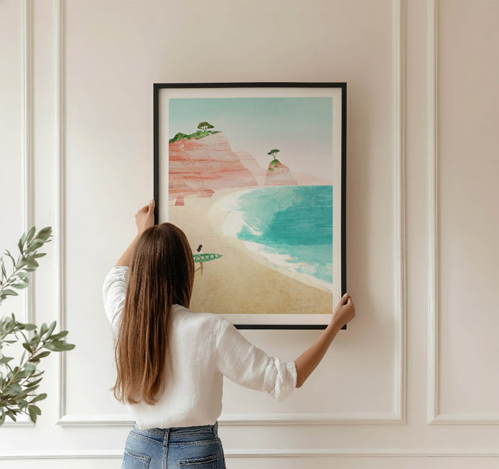 Person hanging a painting of a beach scene on a wall.