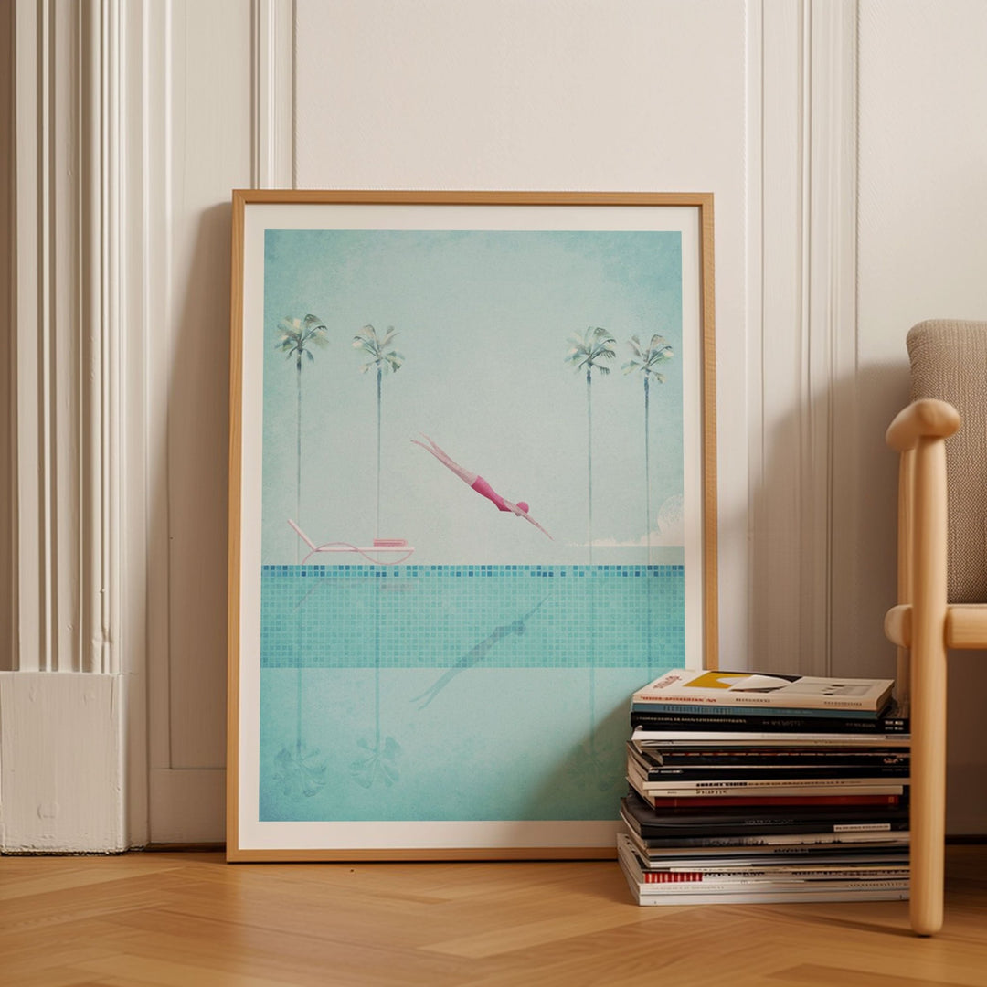 Artwork of a pool scene with palm trees on a wall above a stack of books.
