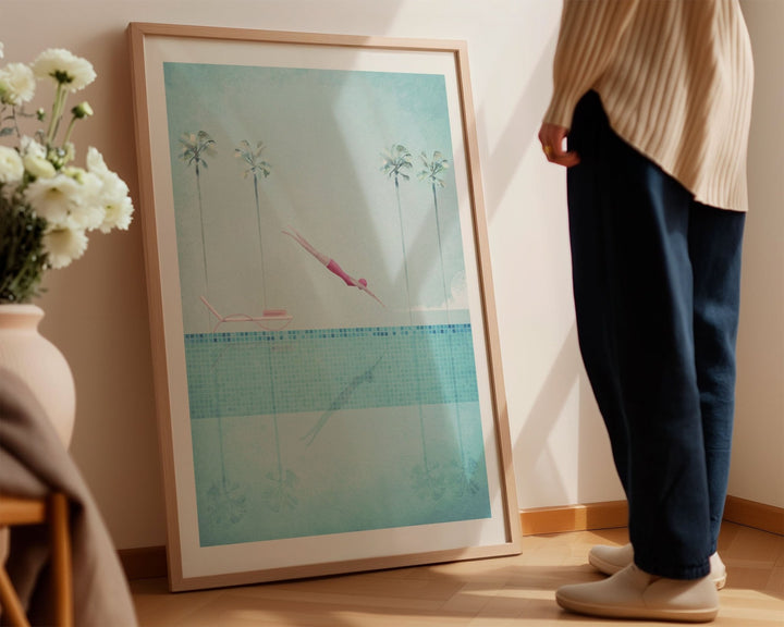 Person standing next to an artwork on a wall with flowers and a chair in the foreground.