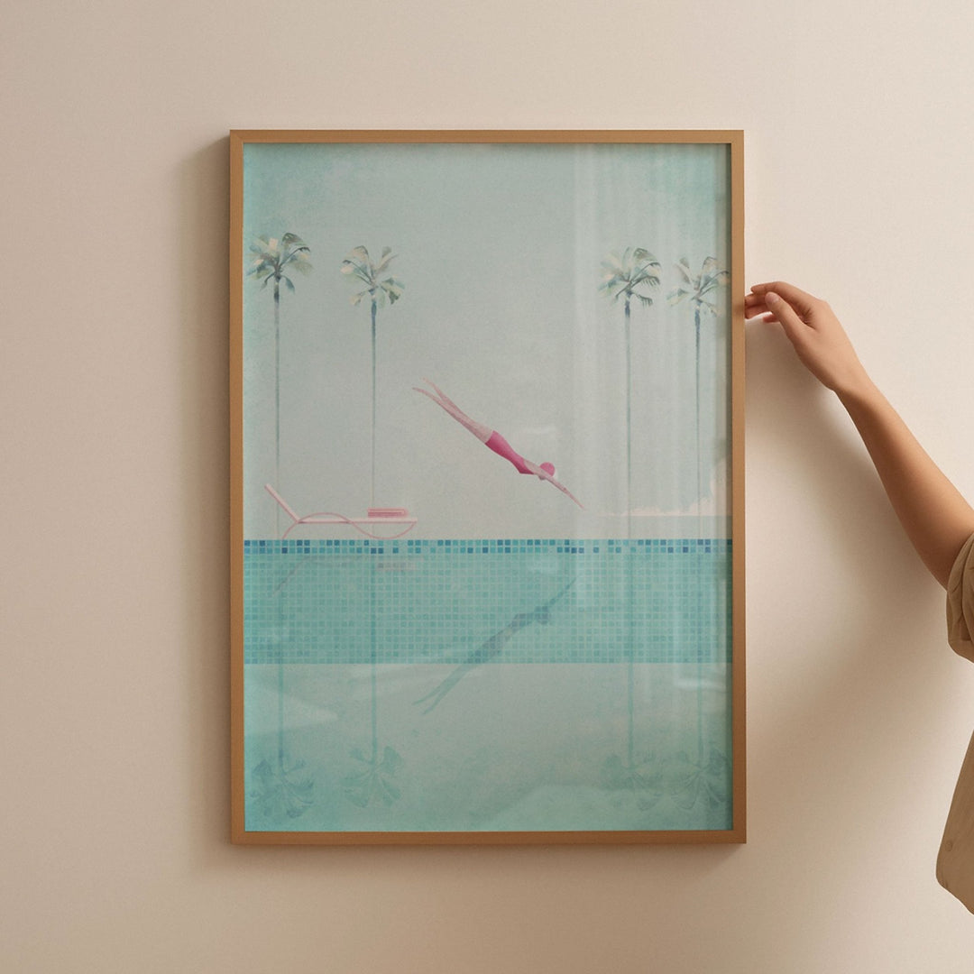Artwork of a pool scene with palm trees and a person in a pink swimsuit, held by a hand against a beige wall.