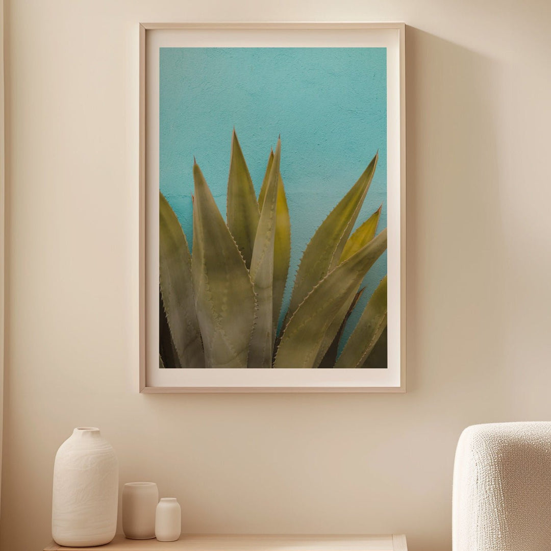 Artwork of a plant on a wall above a wooden side table with decorative items.