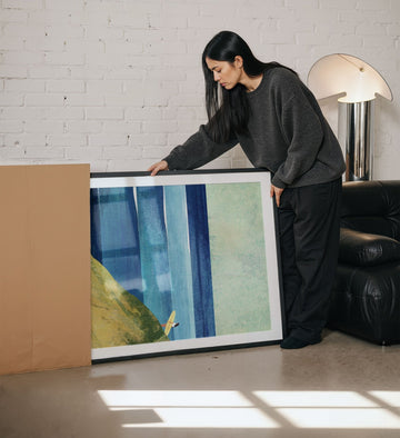 Woman holding an artwork in a living room.