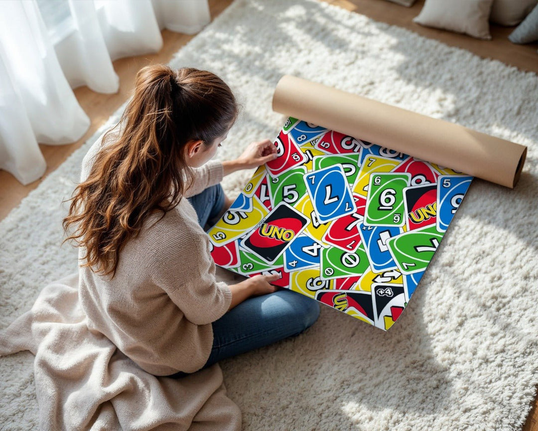 Person unrolling colorful UNO card game packaging on a light-colored rug.
