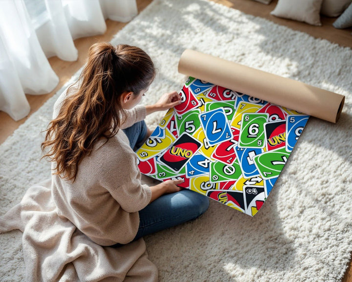 Person unrolling colorful UNO card game packaging on a light-colored rug.