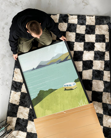 Person unboxing a scenic poster on a checkered rug