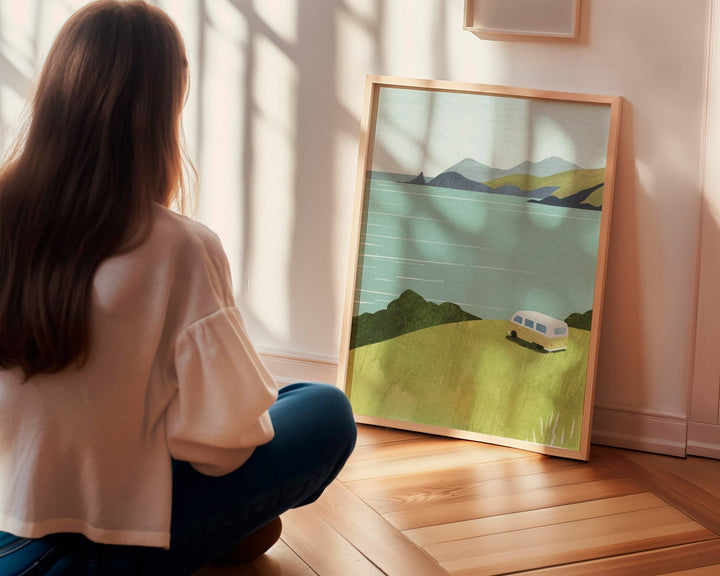 Woman looking at landscape painting of a mountain and camper van on a wooden floor.