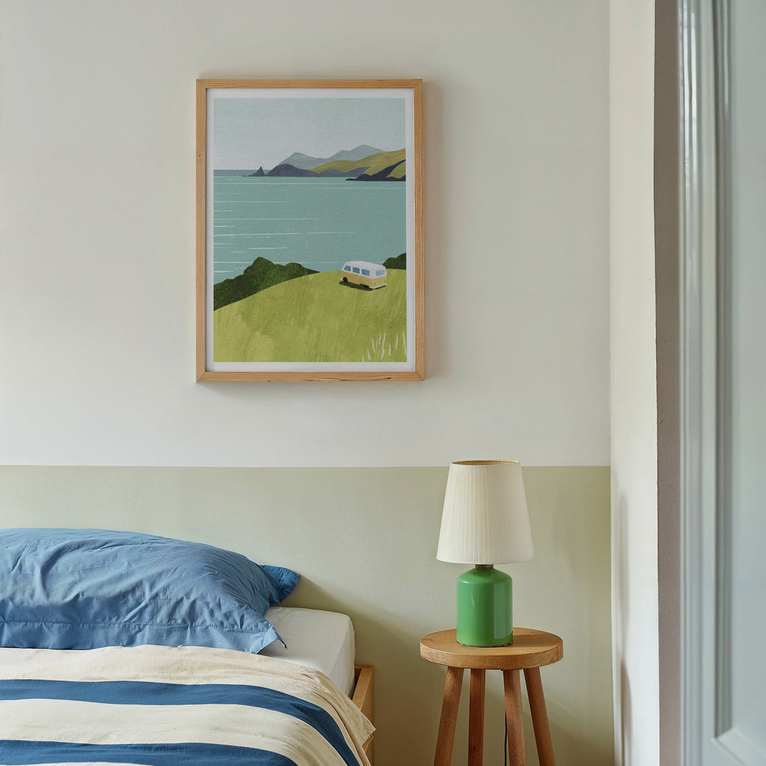 Artwork of a landscape with a lake and mountains above a bed in a bedroom.
