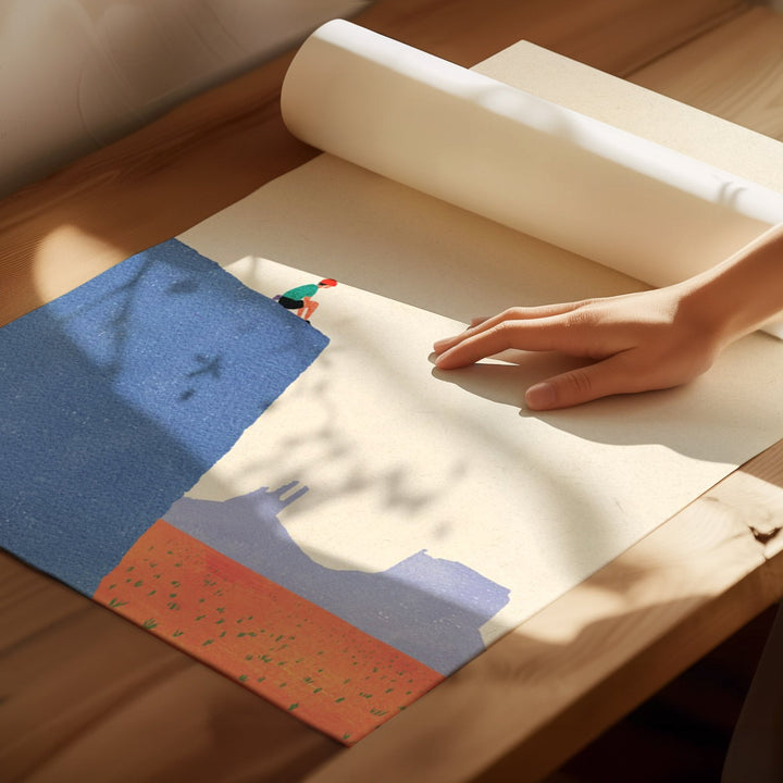 Hand rolling out a large sheet of paper with a colorful landscape design on a wooden surface.