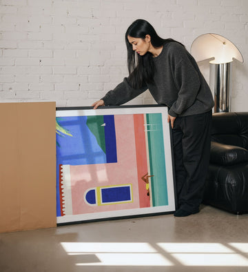 Woman holding a colorful abstract painting in a living room.