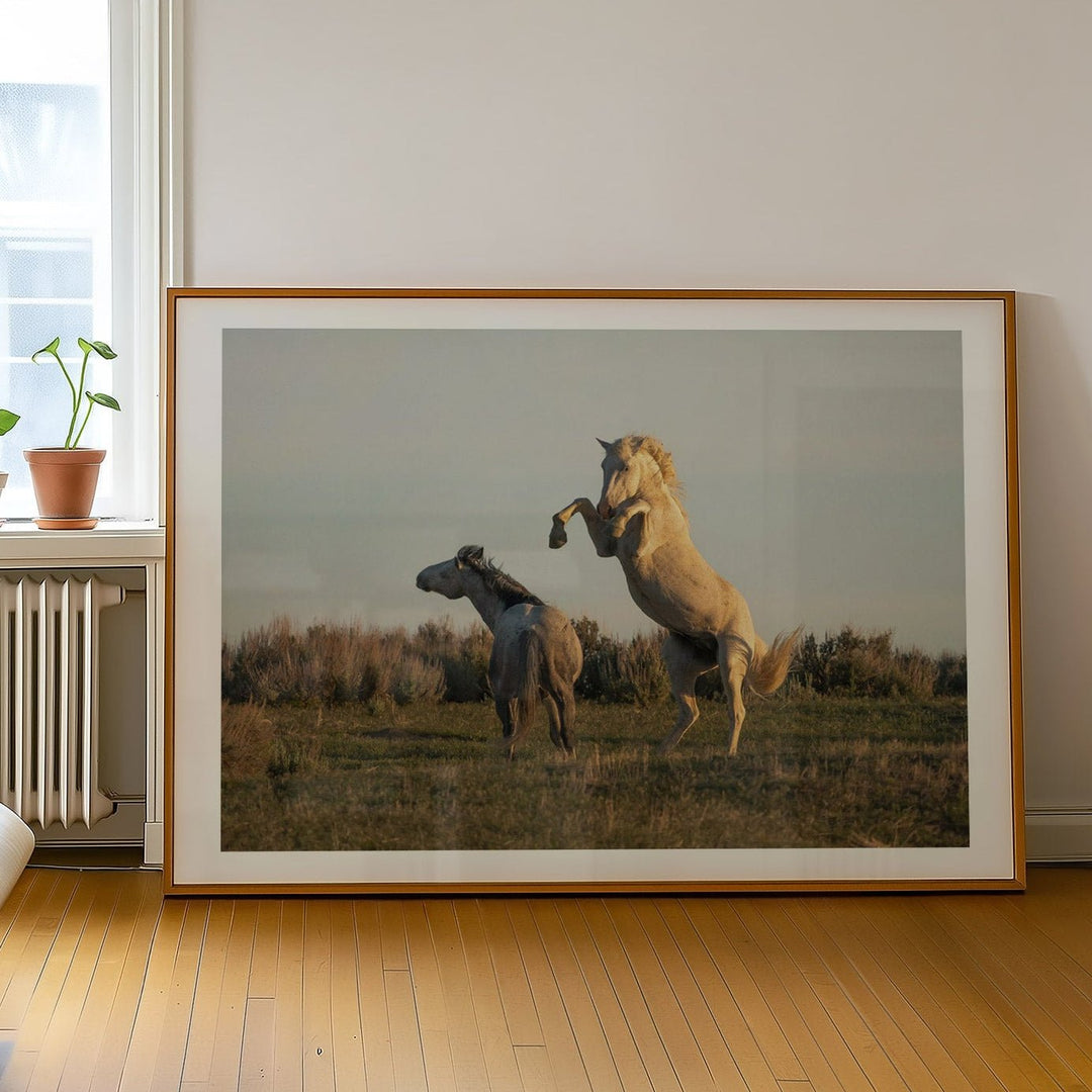 artwork of two horses in a field on a wall in a room with a bed and window.